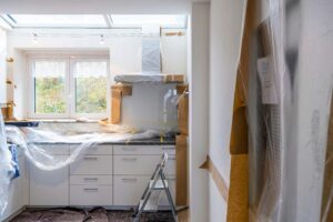 Kitchen renovation in older Alberta home with cabinets covered in plastic sheeting before potential asbestos testing